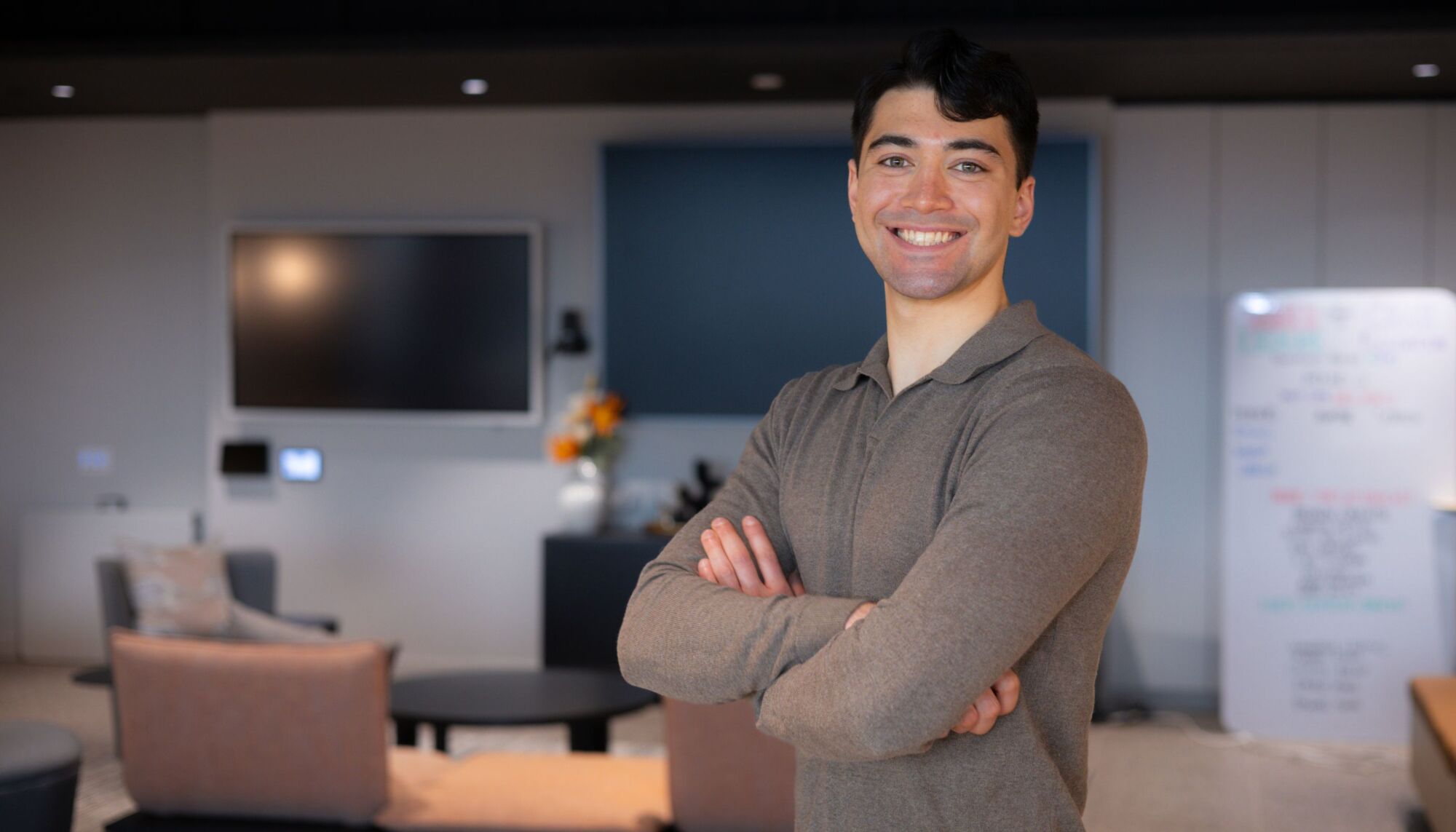Man with arms crossed wearing blow collared sweater smiling at camera with background blurred