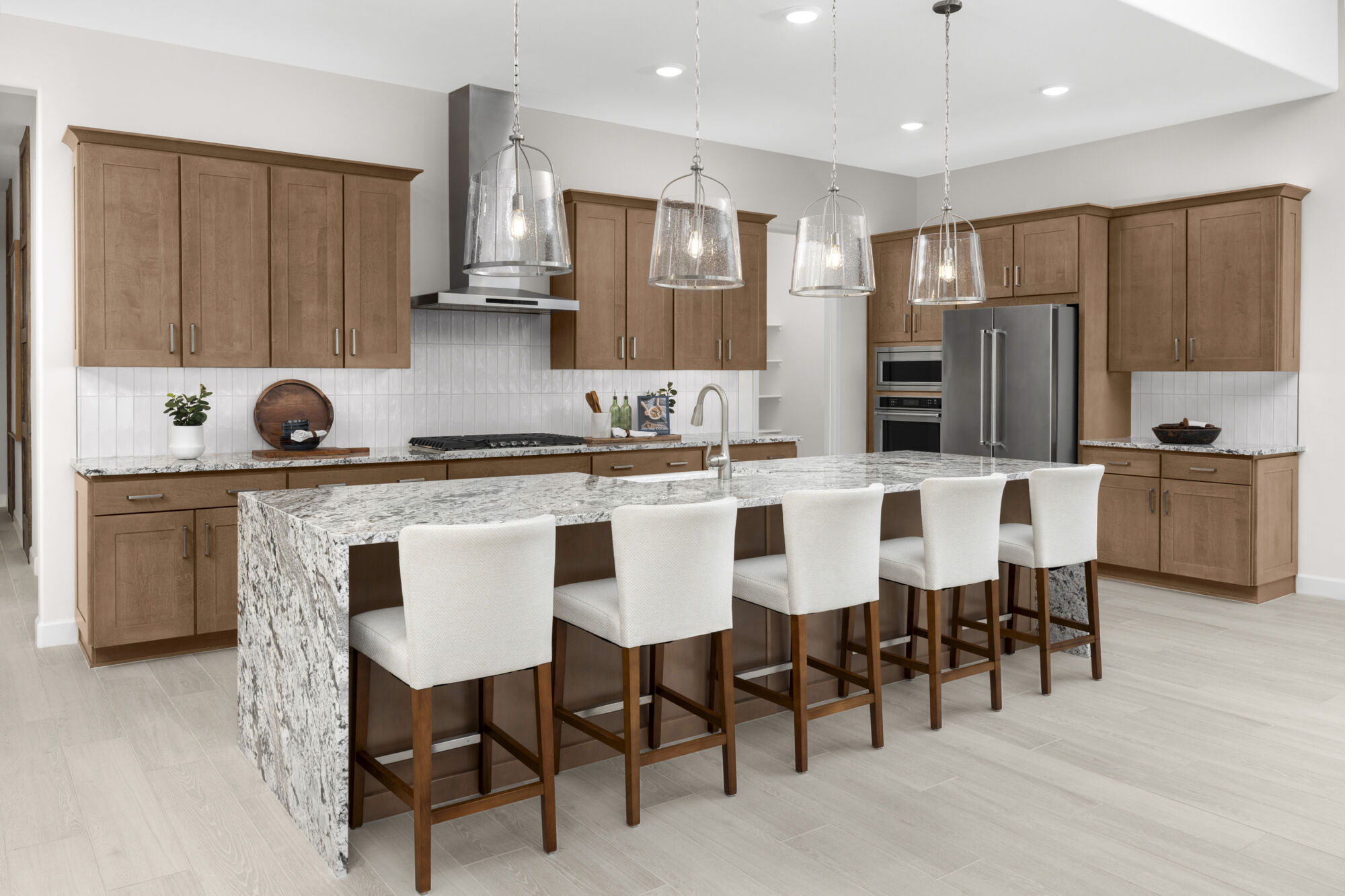 L-Shaped Kitchen with pendant light, light wood cabinets, refrigerator, cooktop, wood flooring and oven