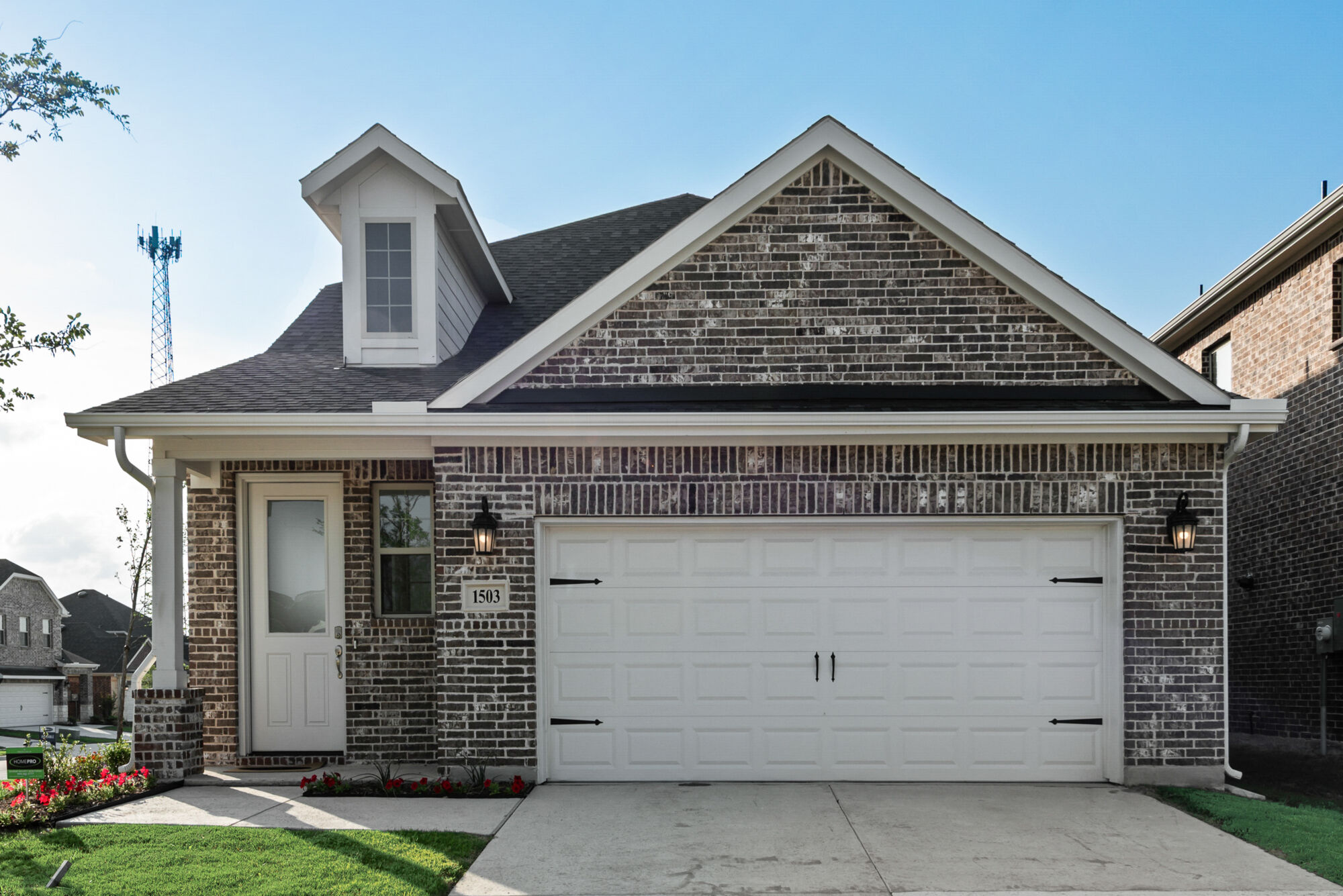 2 story brick home with covered front patio, 2 car garage, landscaping, white accents and windows