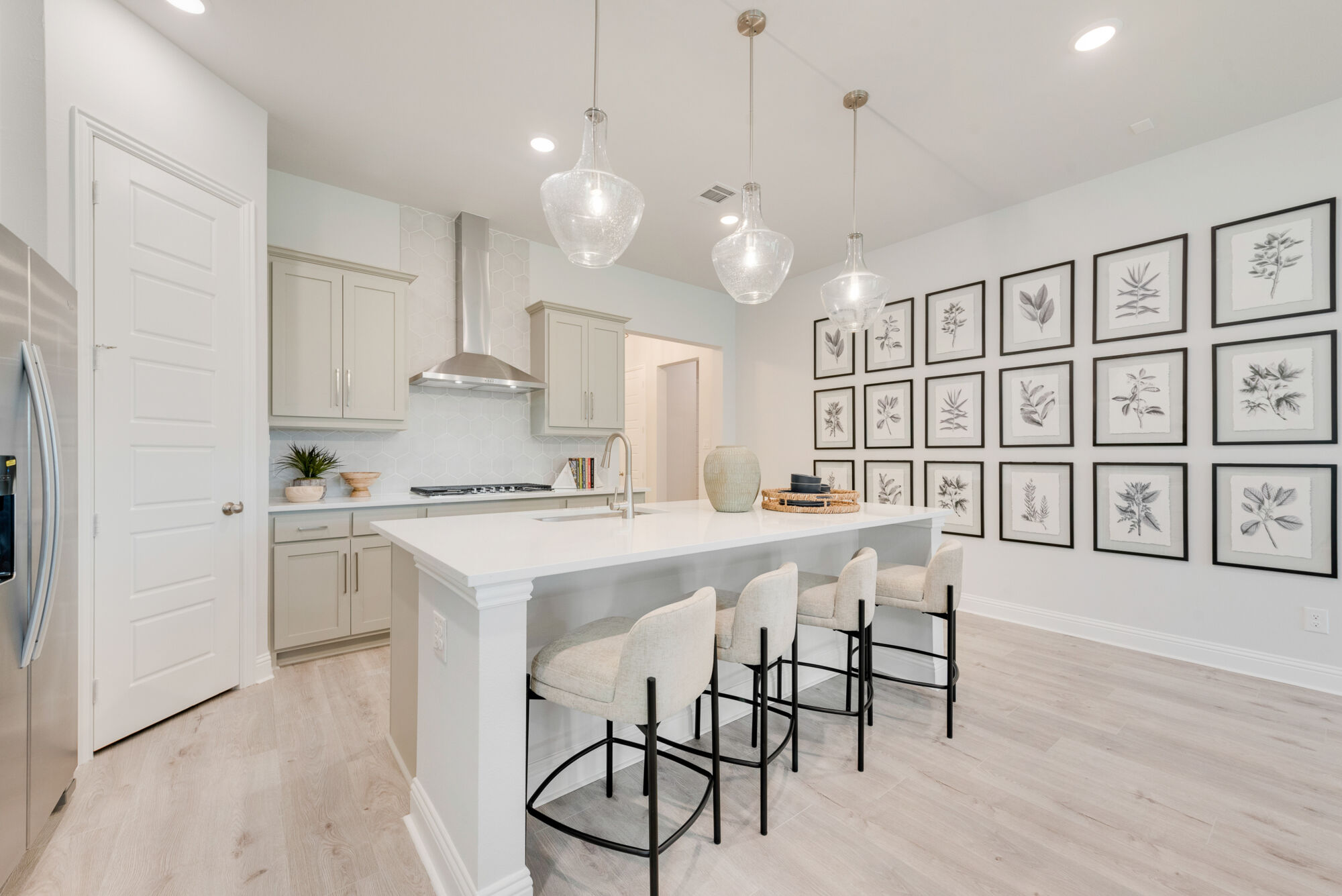 L-Shaped Kitchen with pendant light, painting, door, cooktop, white cabinets, wood flooring and refrigerator