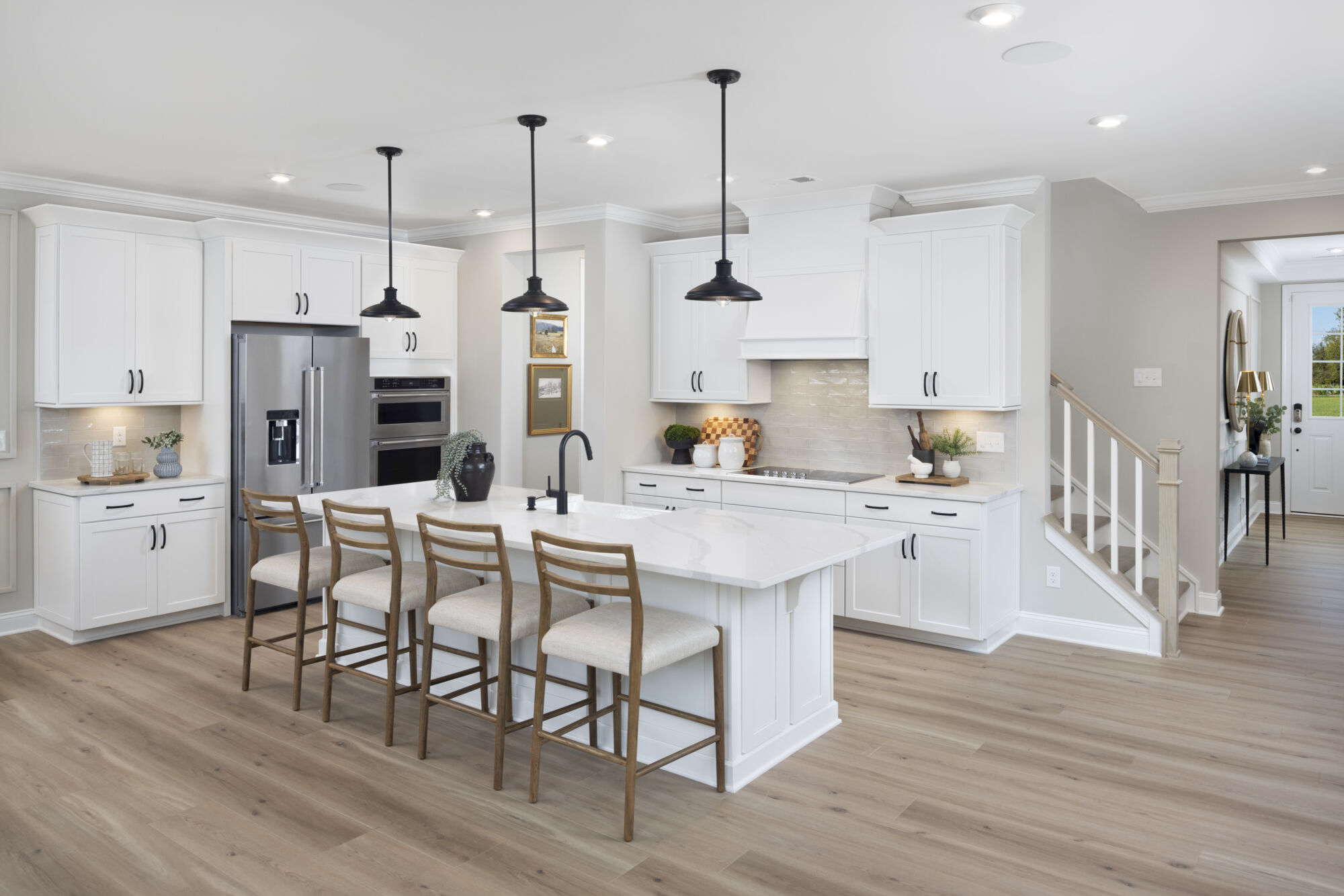 L-Shaped Kitchen with refrigerator, pendant light, oven, cooktop, door, painting, white cabinets and wood flooring