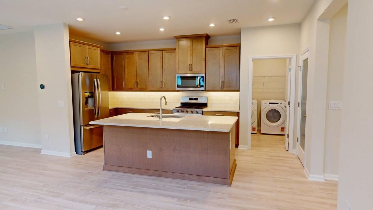 L-Shaped Kitchen with refrigerator, washer-dryer, range, wood flooring and light wood cabinets
