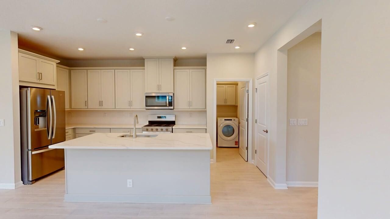 U-Shaped Kitchen with door, white cabinets, refrigerator, range, wood flooring and washer-dryer