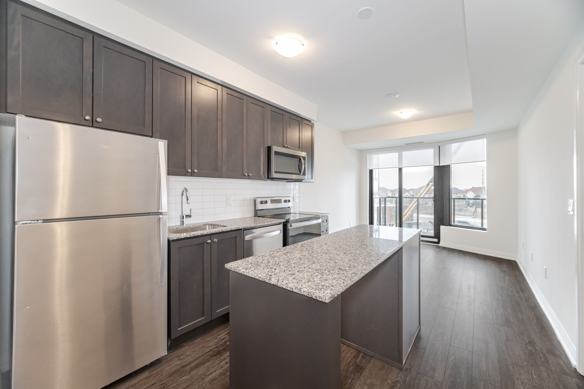 Condo Kitchen with dark cabinetry, stainless steel appliances, kitchen island and granite countertop