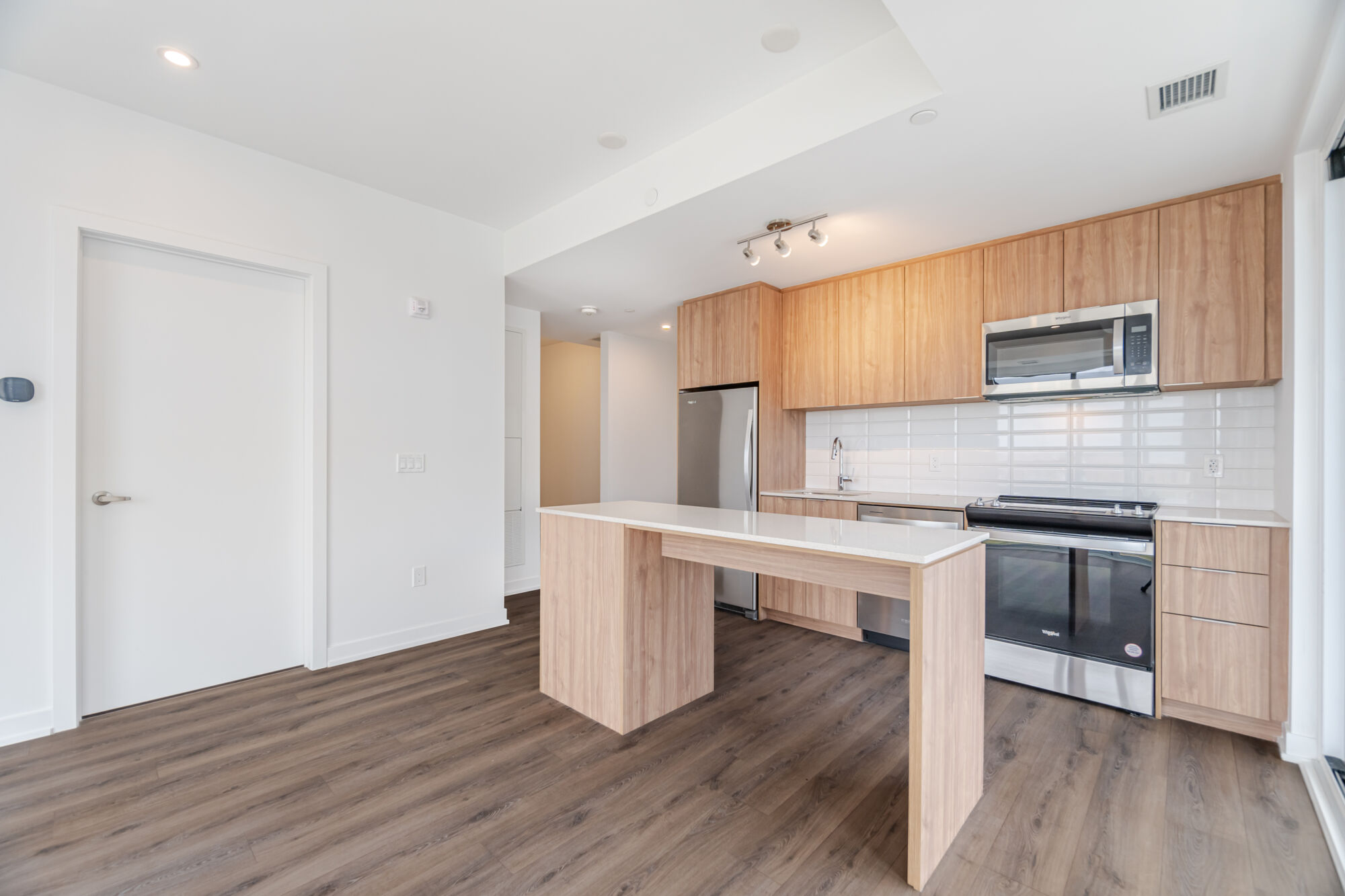 Condo Kitchen with wood grain cabinetry, stainless steel appliances, kitchen island and quartz countertop. 