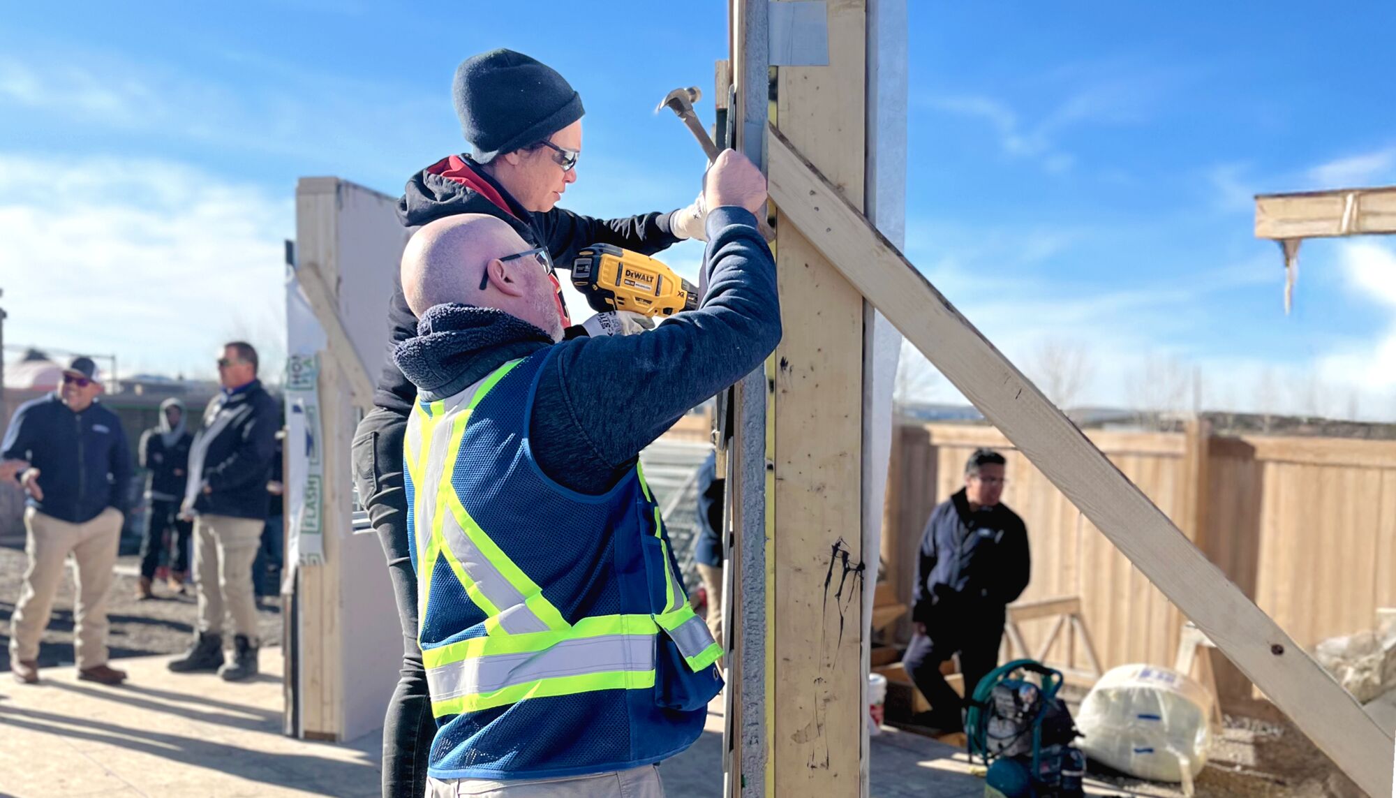 Two people work on building a frame outdoors.