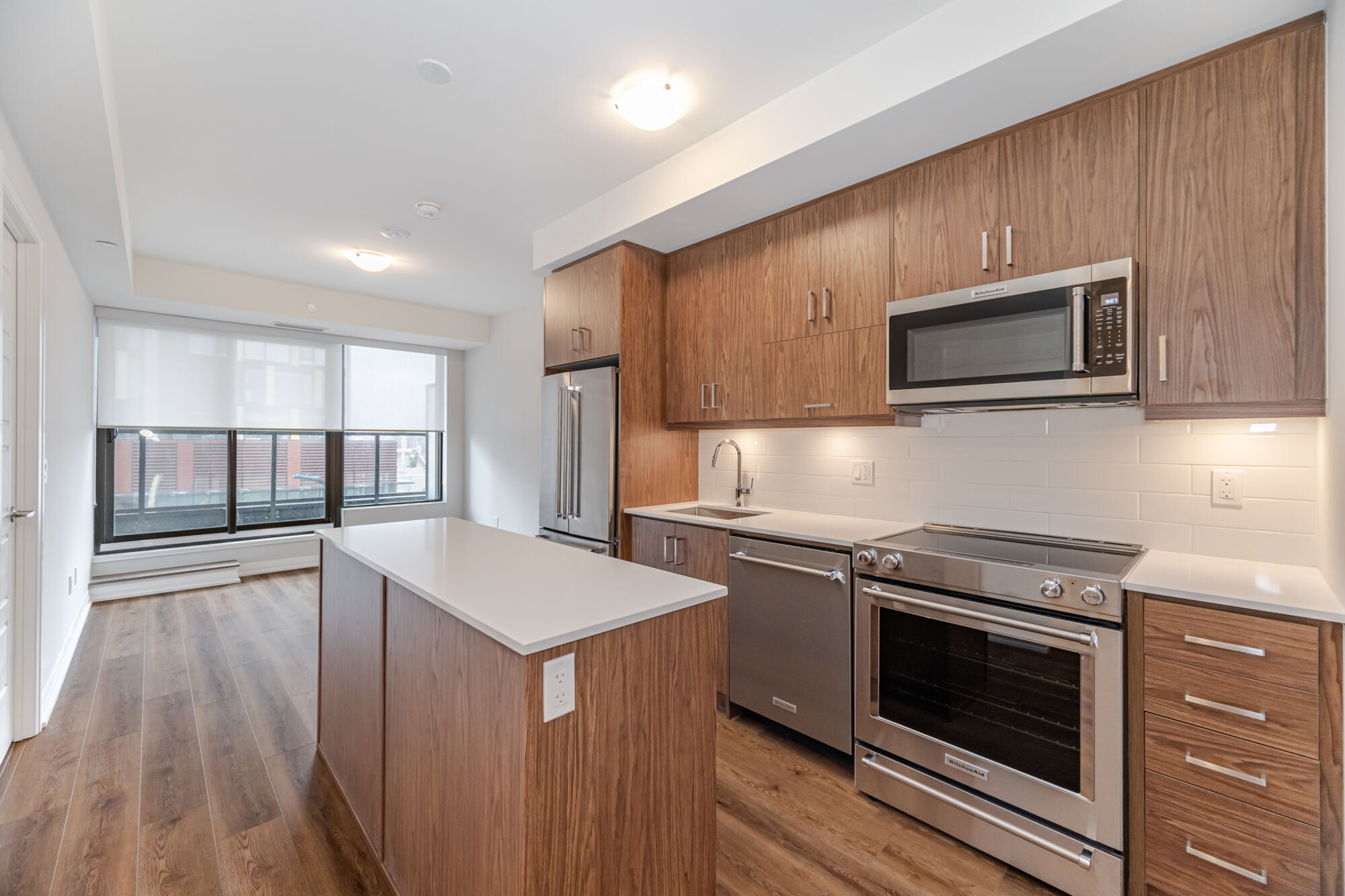 Condo kitchen with medium wood cabinets, kitchen island, quartz countertop and stainless steel appliances. 