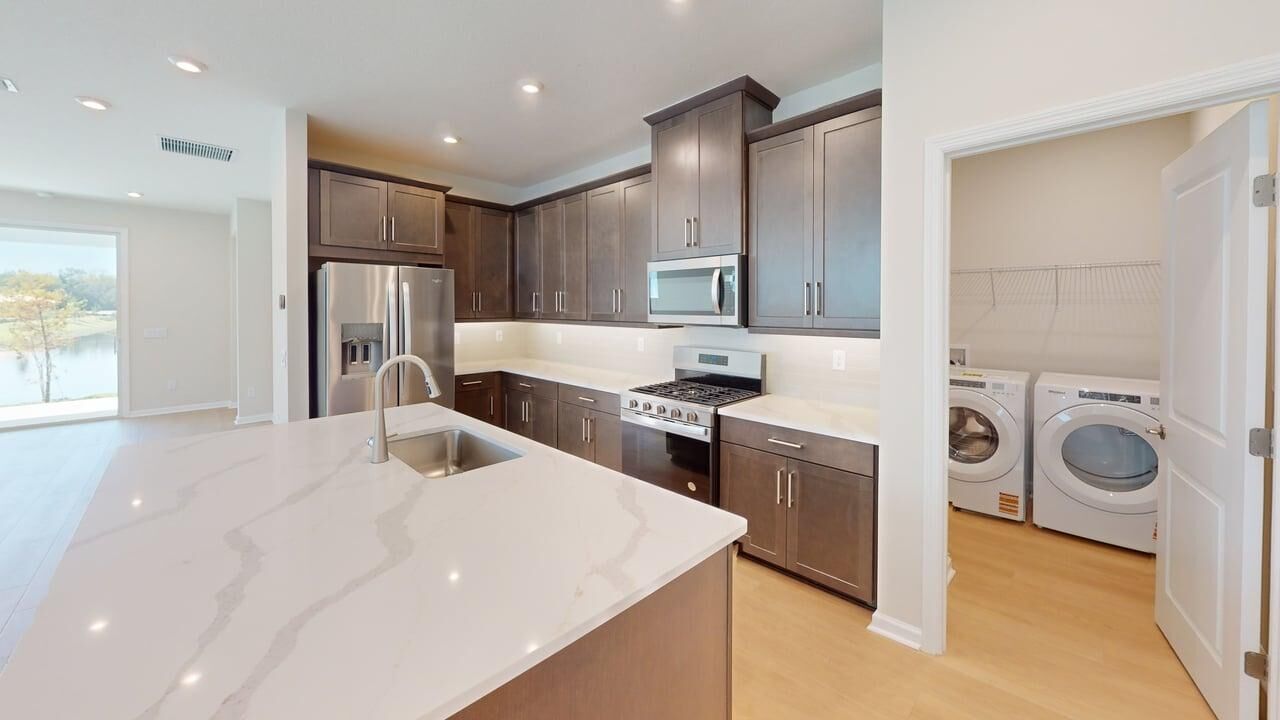 L-Shaped Kitchen with door, refrigerator, washer-dryer, dark wood cabinets, range and wood flooring