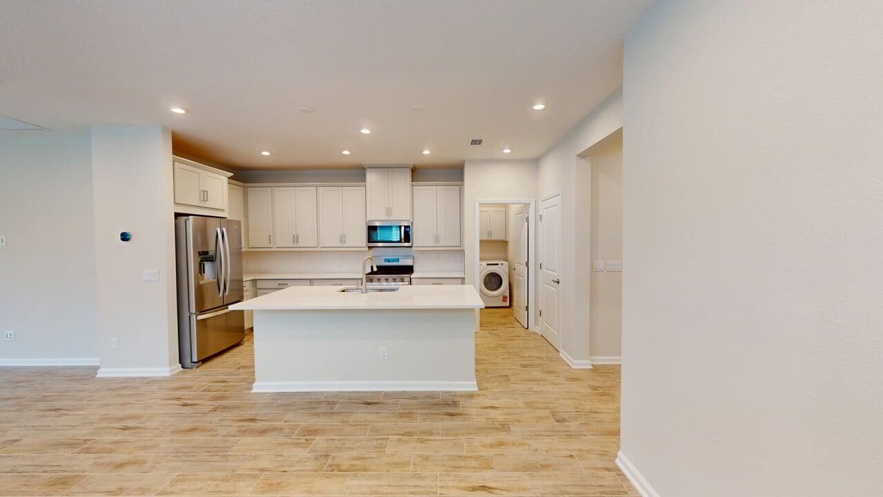  Kitchen with refrigerator, door, wood flooring, white cabinets, washer-dryer and range