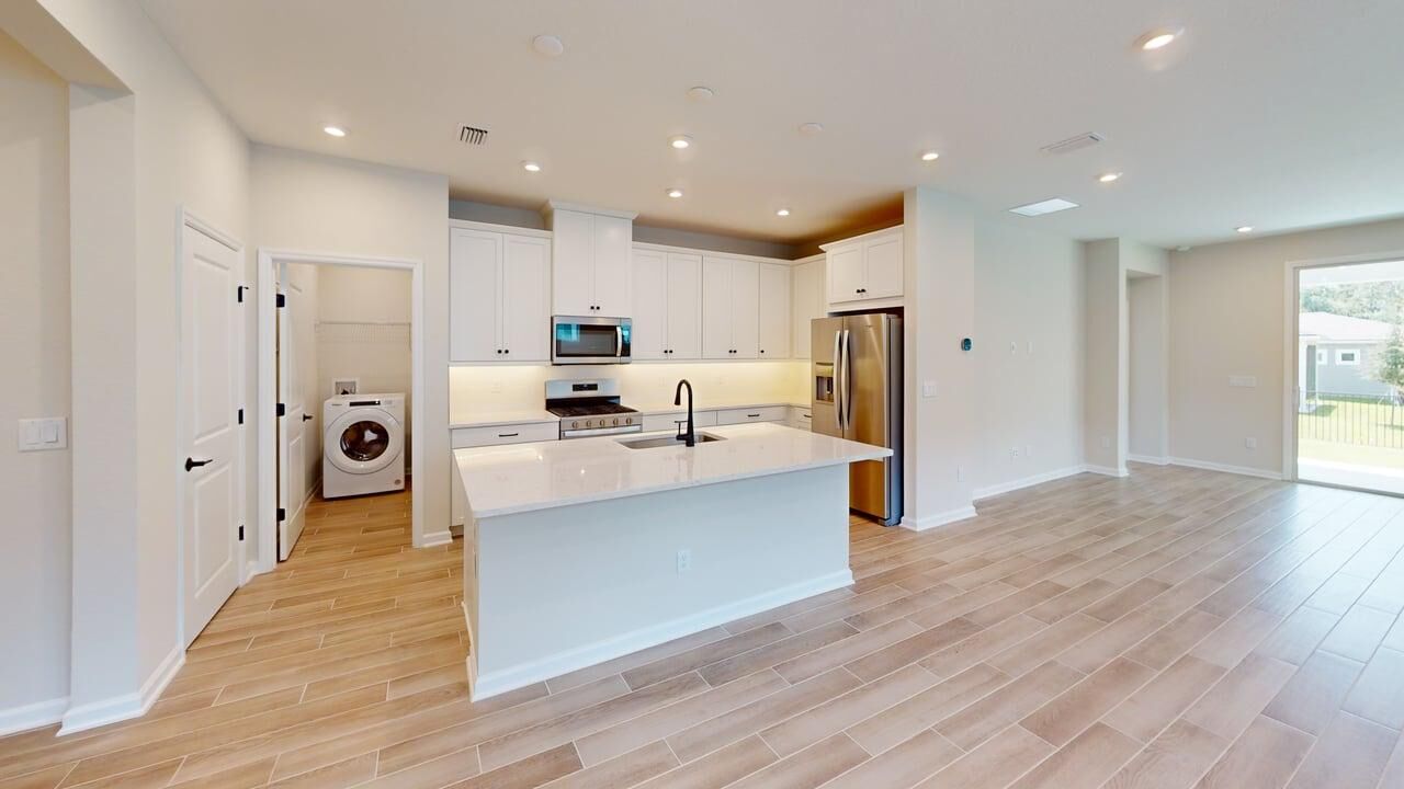  Kitchen with door, white cabinets, refrigerator, range, washer-dryer and wood flooring