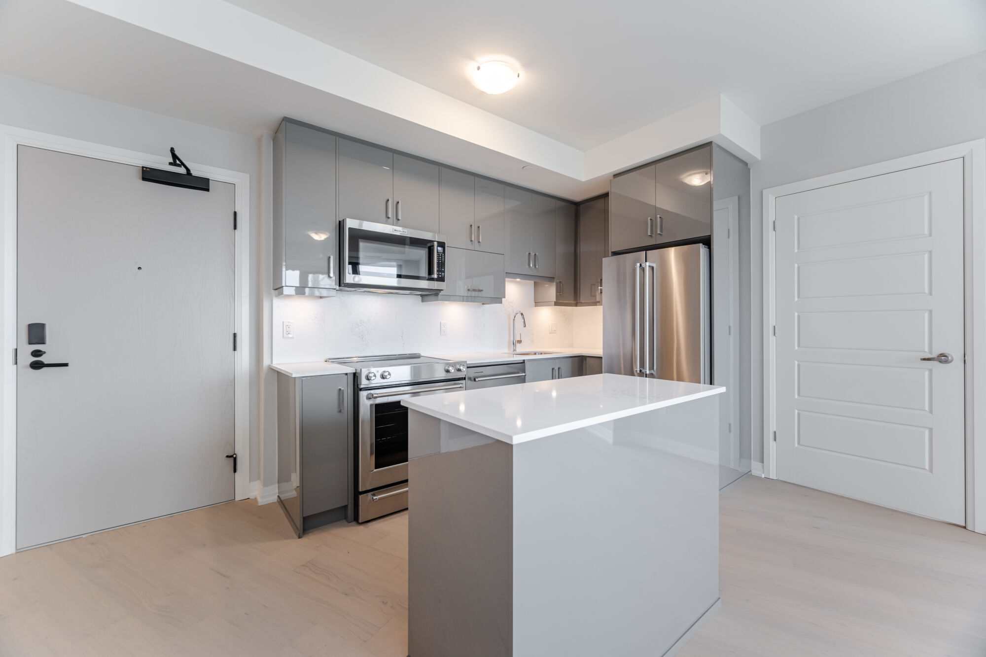 Condo kitchen with grey cabinetry, stainless steel appliances, kitchen island and quartz countertops.