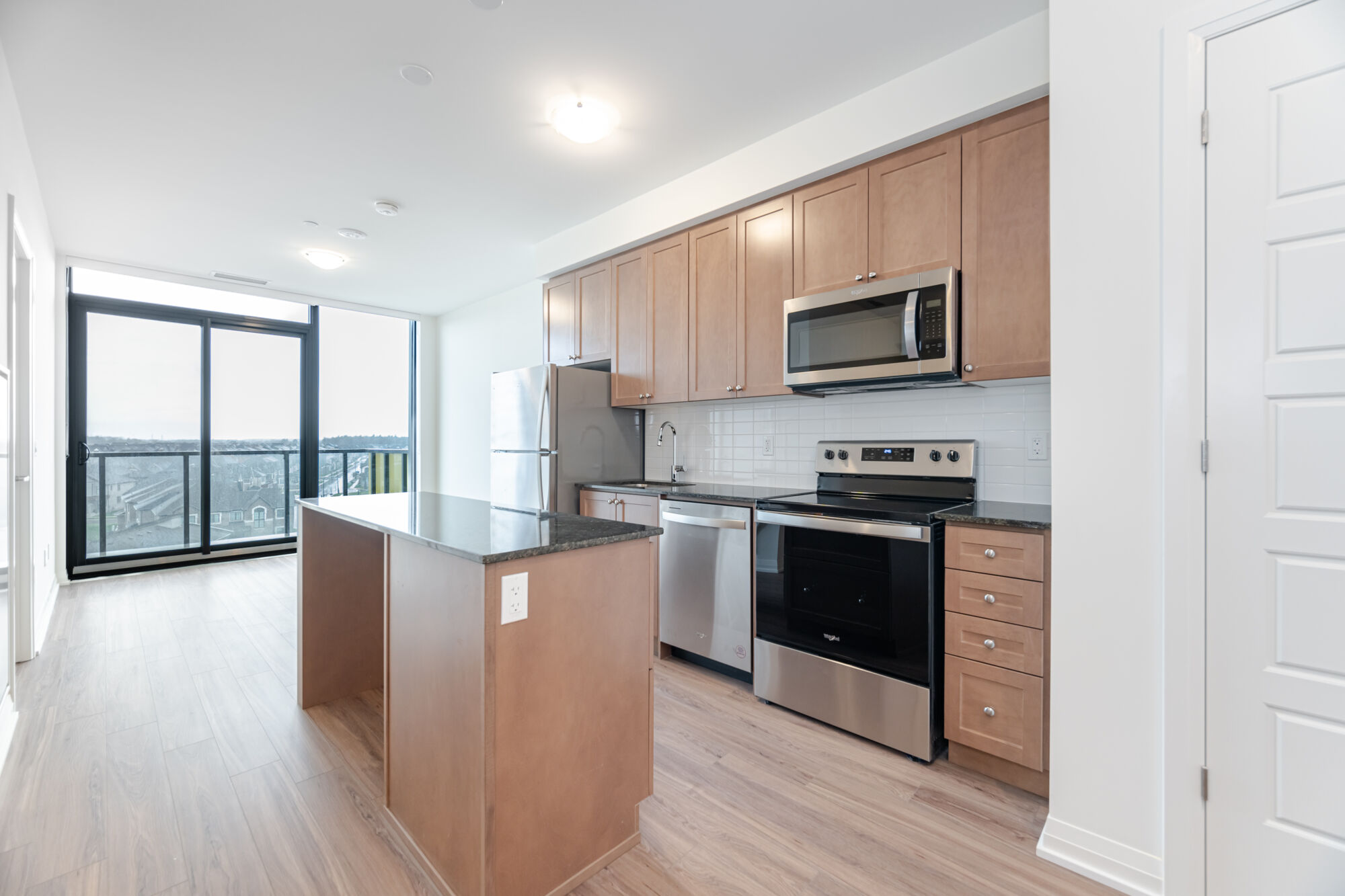 Condo kitchen with light wood-toned cabinetry, stainless steel appliances, kitchen island and granite countertops.
