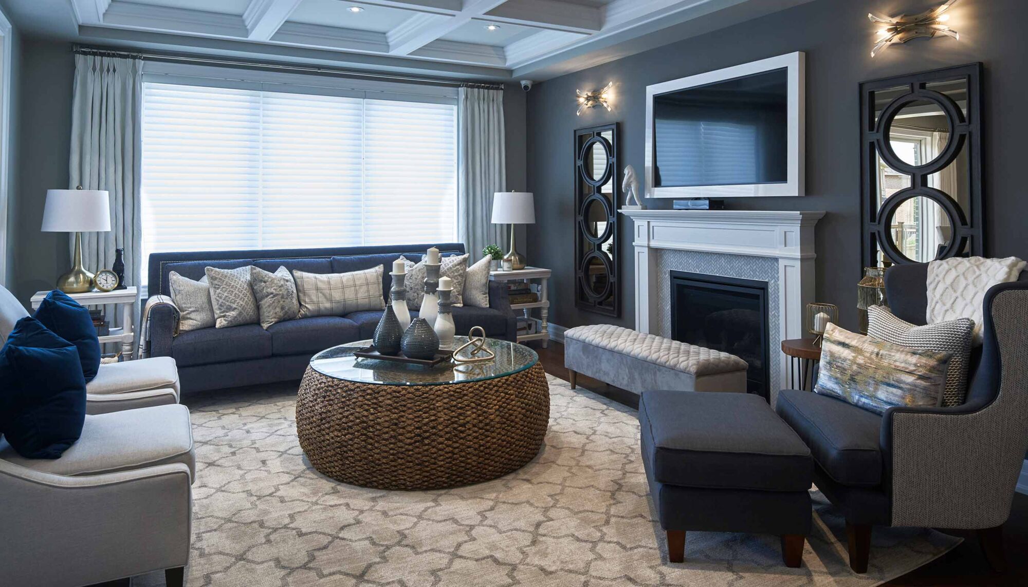 Living room with grey couches, armchairs, and a bench in front of a television and fireplace.