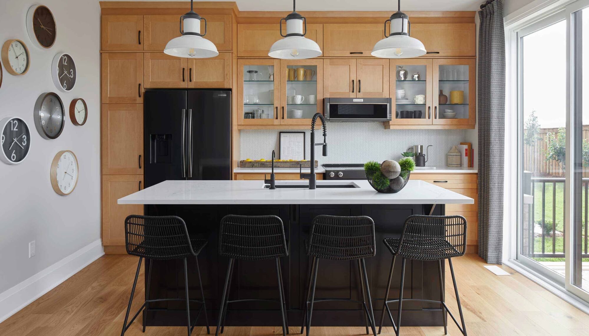 Kitchen with a black and white island, black metal counter stools, and wooden cabinets.