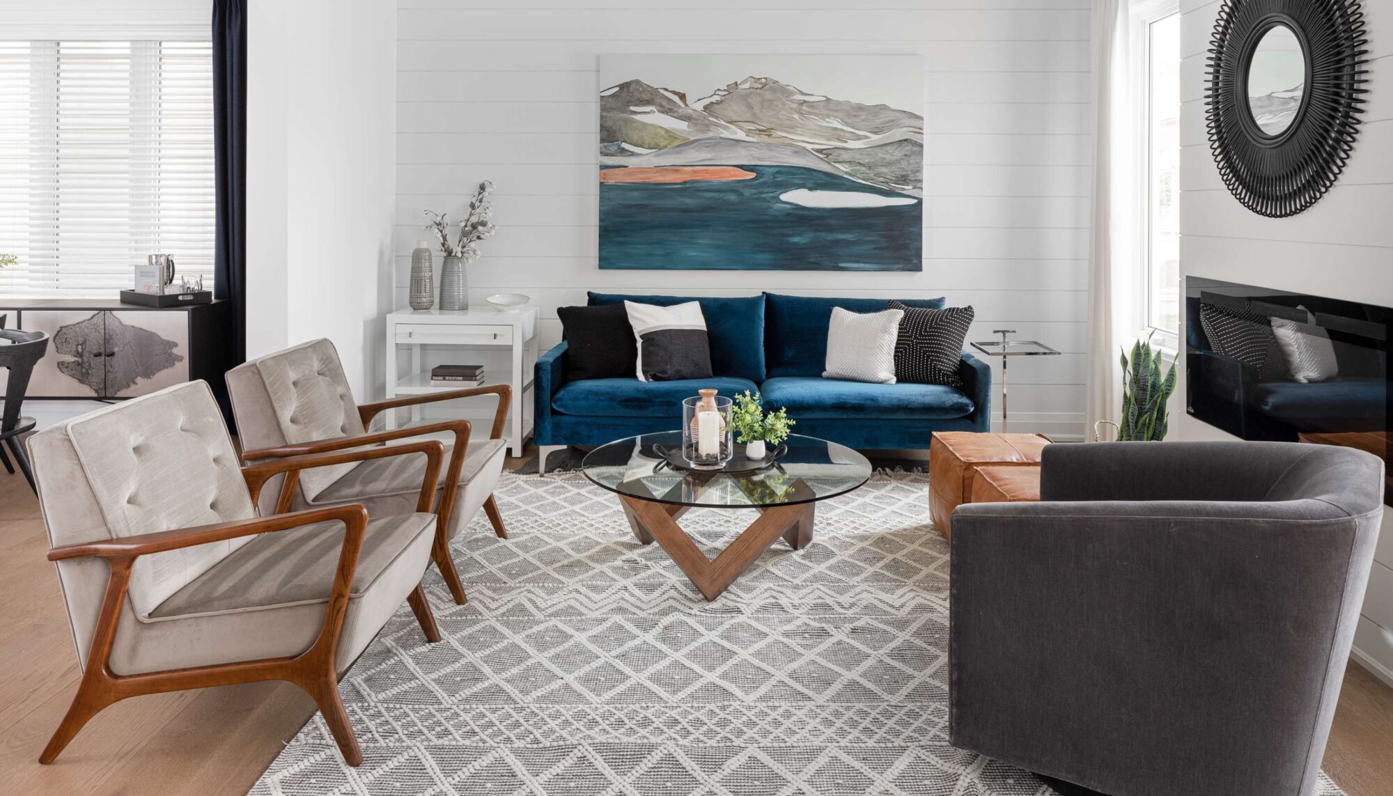 Greatroom with multiple chairs, a colorful painting and a circular mirror on the right side of the wall. 