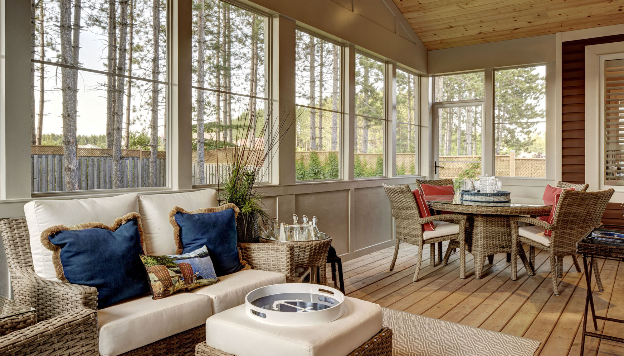 A room with windows surrounding it and a wicker chair and wicker dinning set on wooden floors. 