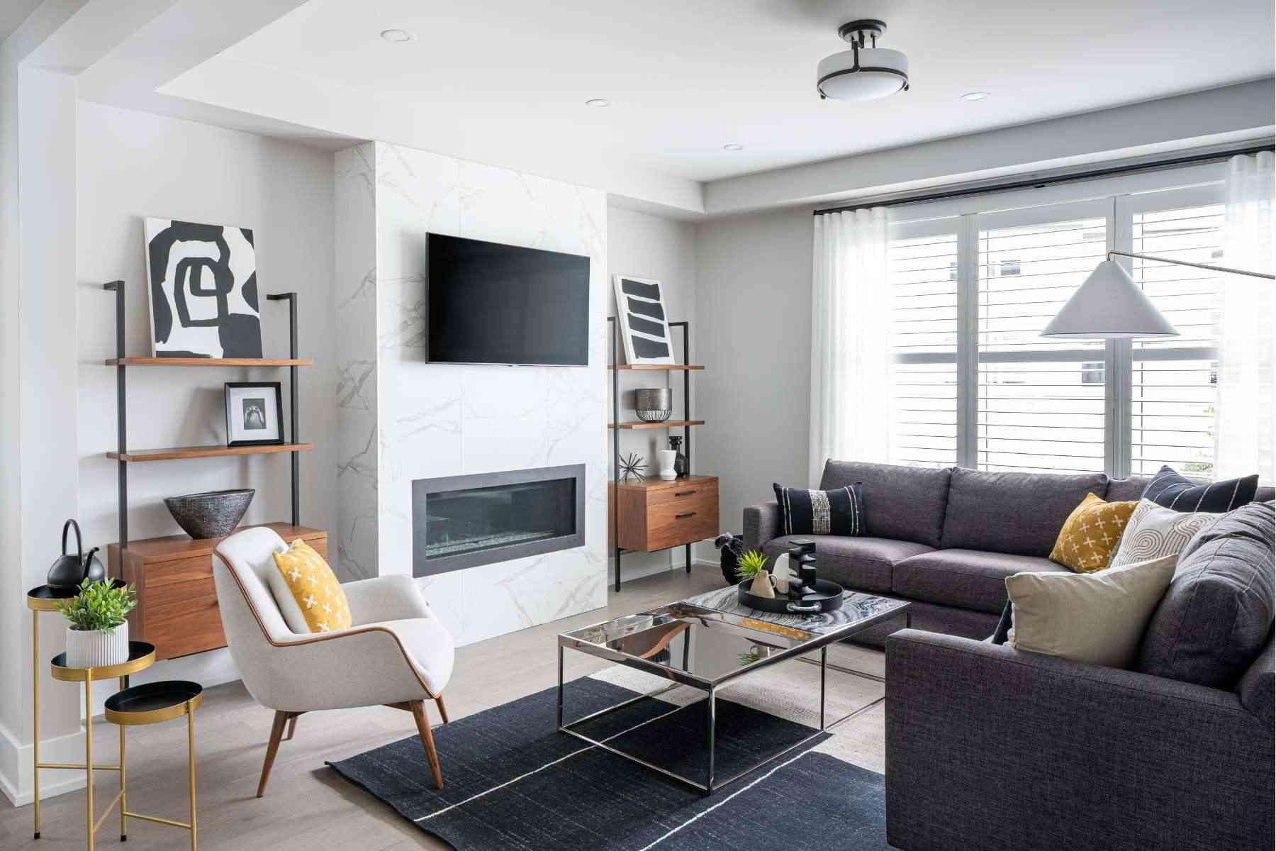 A living room with an L-shaped grey couch and a marble coffee table in front of a television and fireplace.
