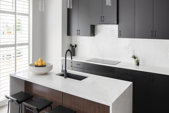 Kitchen with a white marble island, black counter stools, and black cabinets.