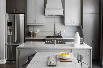 Kitchen with a white marble island, a white grid wall, and white and brown cabinets.