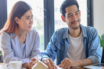 A man and woman looking and smiling at another person which they gesture with their hands.
