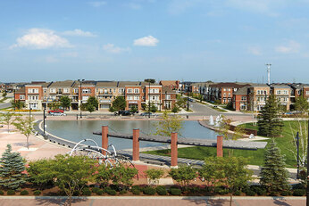 Large pond surrounded by green trees, houses and a park.