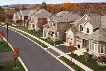 Row of homes on a curved road with red trees in the distance. 