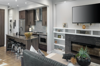 Small kitchen and living room side by side with a TV over some shelving and a staircase in the distance.  