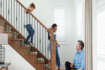 Two children walk down wooden stairs while their father sits at the bottom looking up to the kids