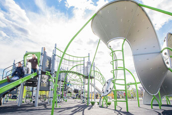 Low view of play structures with child sliding down slide in playground with a blue sky
