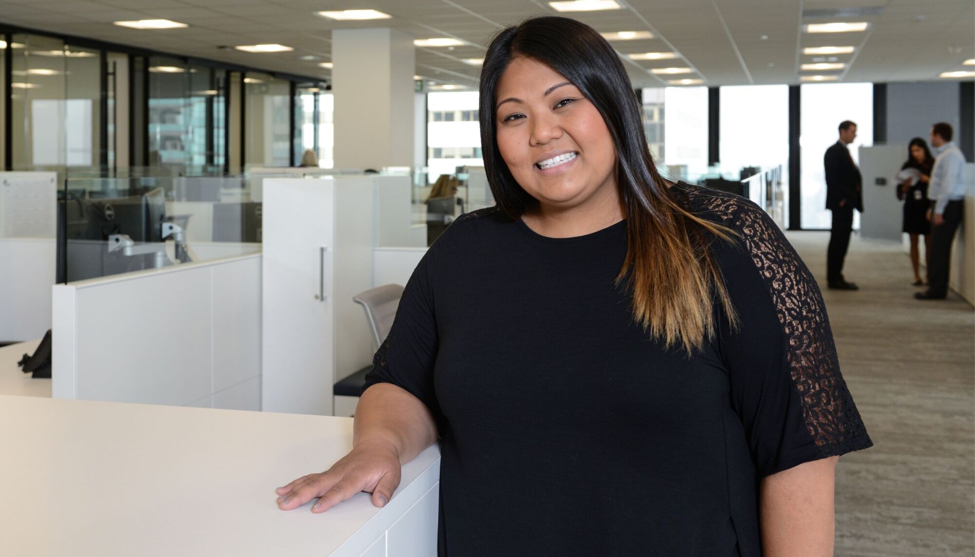 Female in open office area with people behind her while smiling at camera