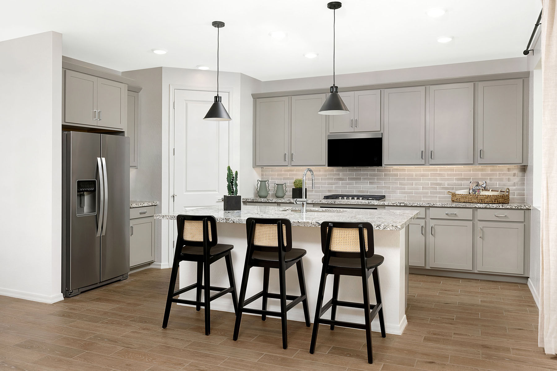 L-Shaped Kitchen with refrigerator, pendant light, window, door, white cabinets, wood flooring and cooktop