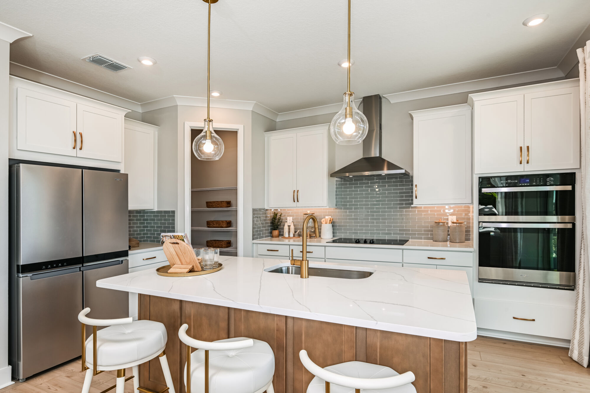 L-Shaped Kitchen with oven, white cabinets, pendant light, refrigerator, cooktop and wood flooring